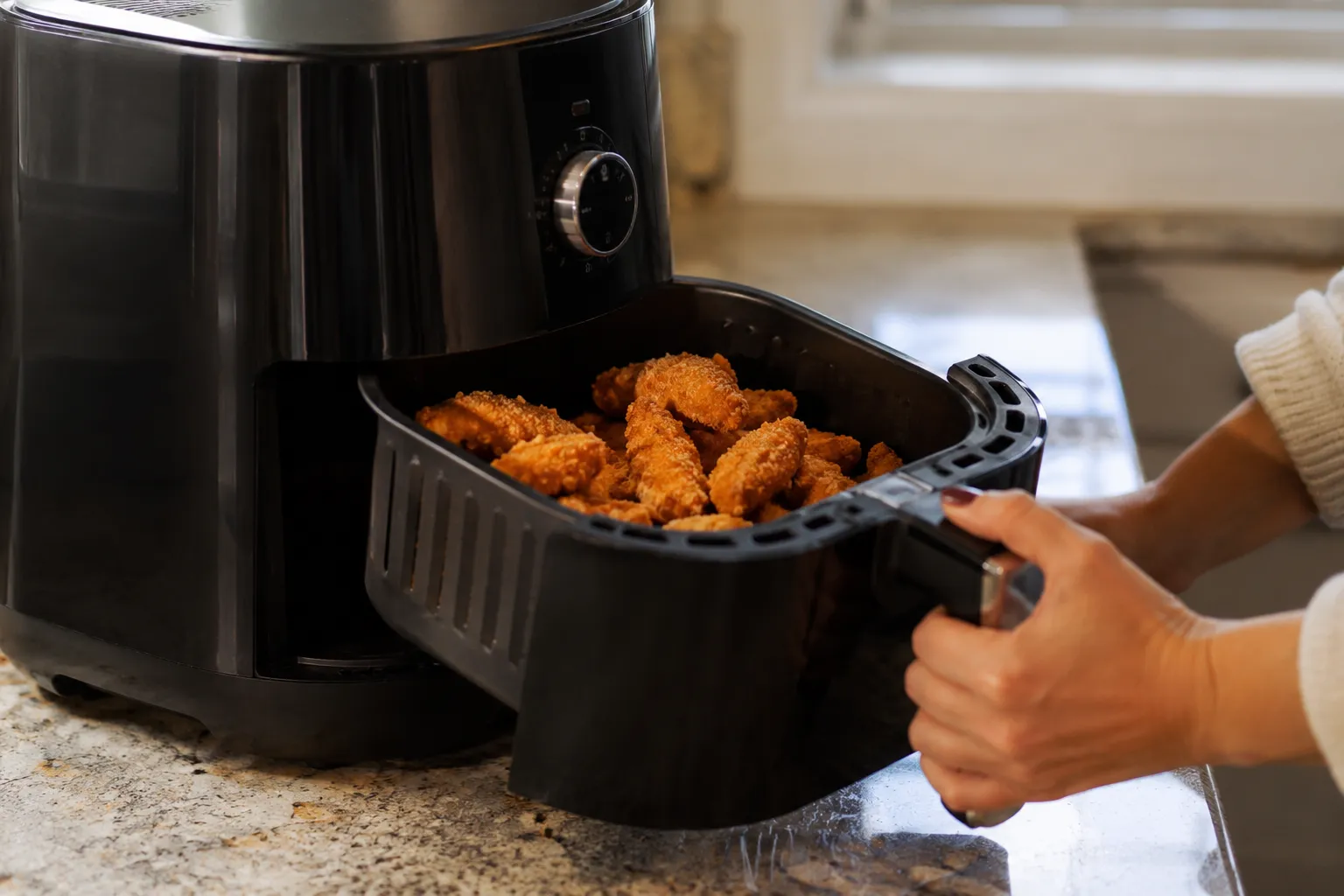pulling a basket of crispy chicken out of an air fryer